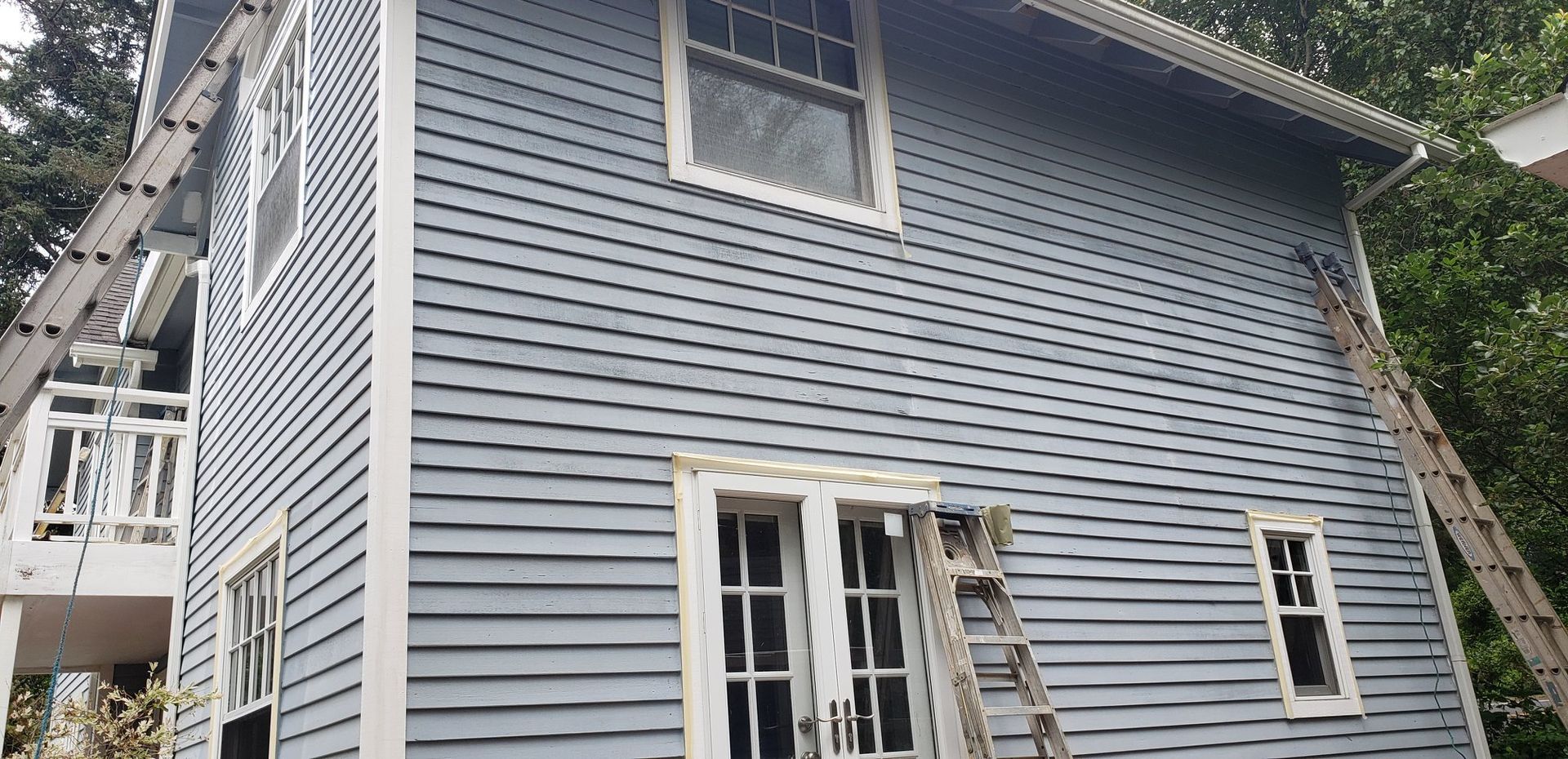 A blue house with a ladder on the side of it is being painted.
