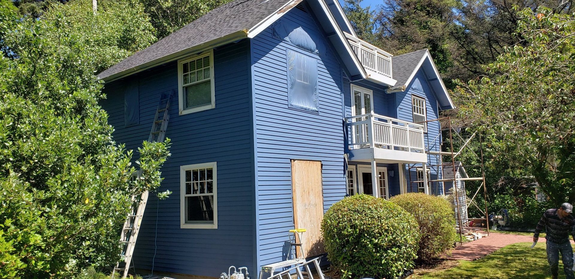 A blue house with a ladder in front of it is being painted.