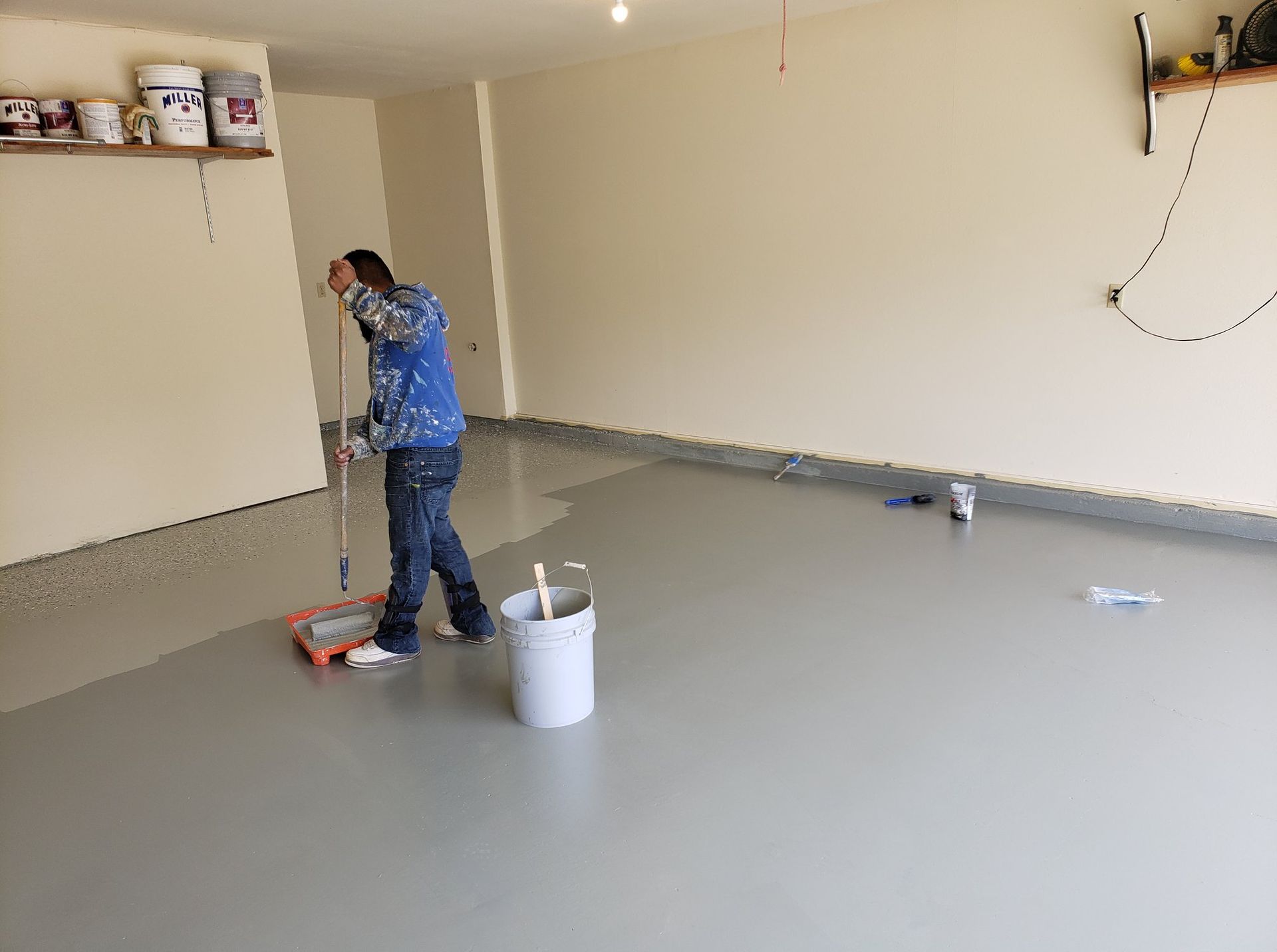 A man is painting the floor of a garage with a roller.