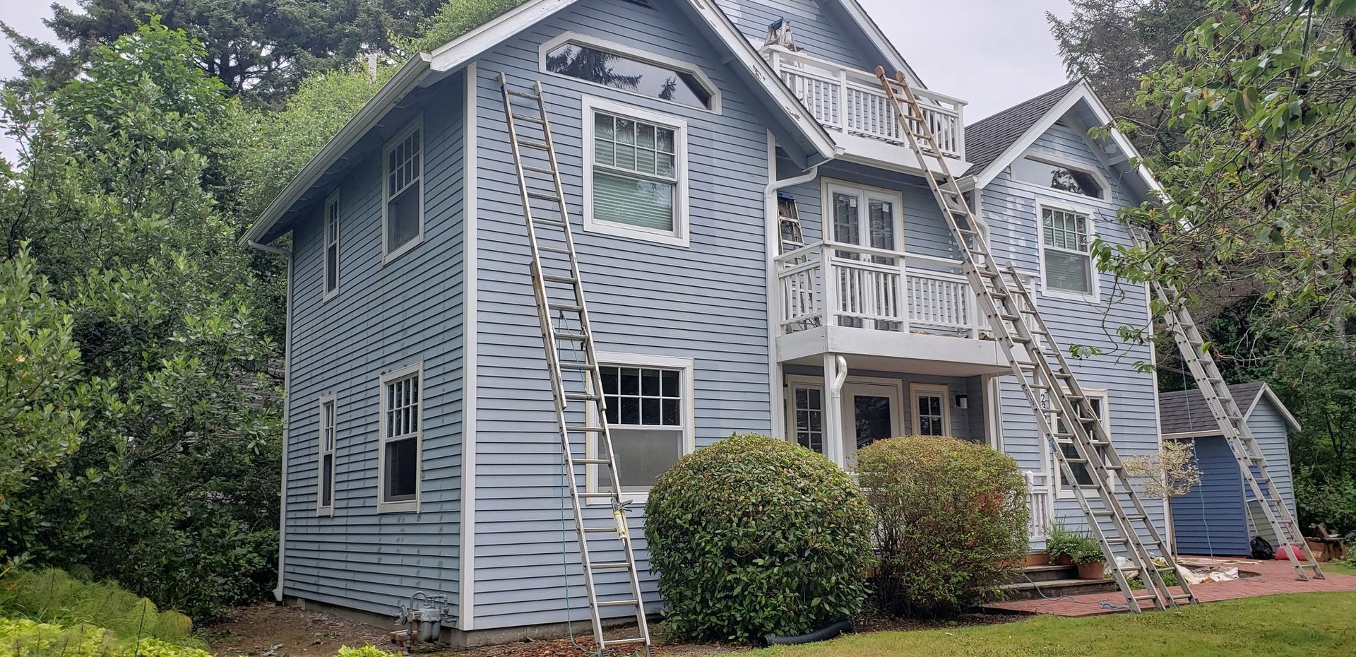 A large blue house with a balcony is being painted.