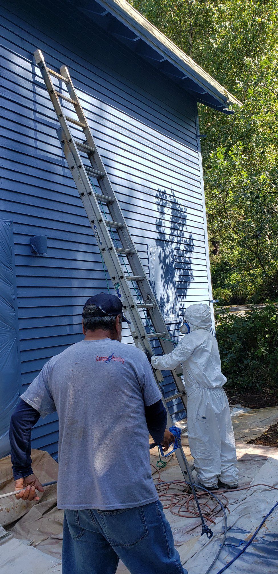 Two men are painting a blue house with a ladder.