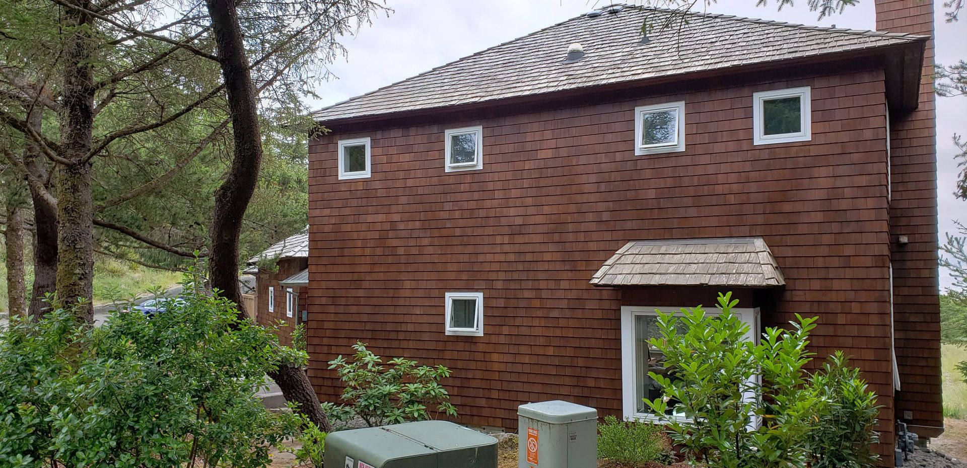 A brick house with a roof and a lot of windows is surrounded by trees.