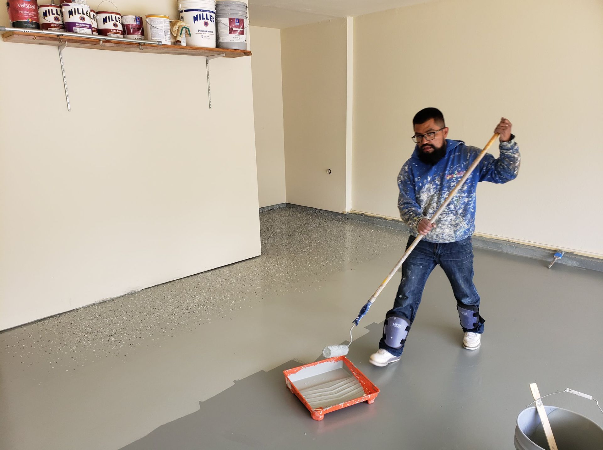 A man is painting a garage floor with a roller.