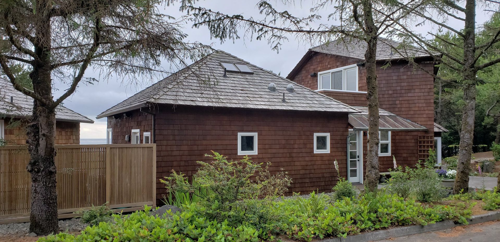 A large brown house with a slate roof is surrounded by trees and bushes.