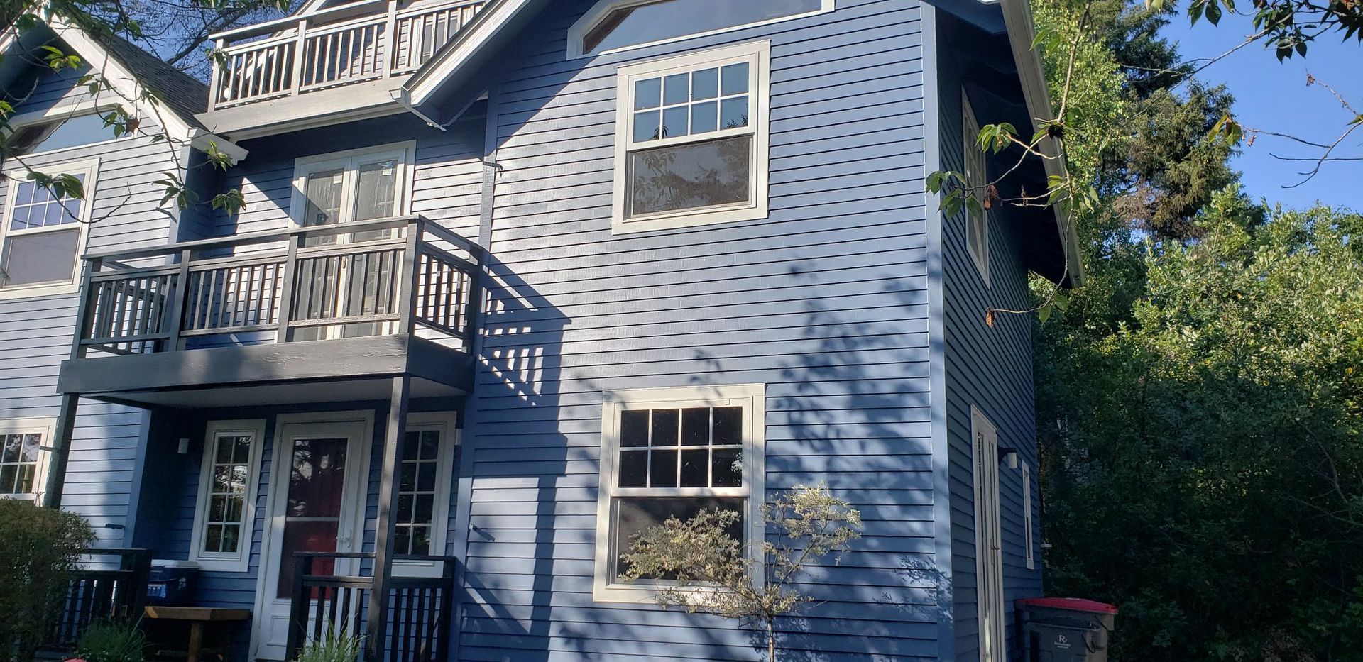 A blue house with a balcony and trees in the background.