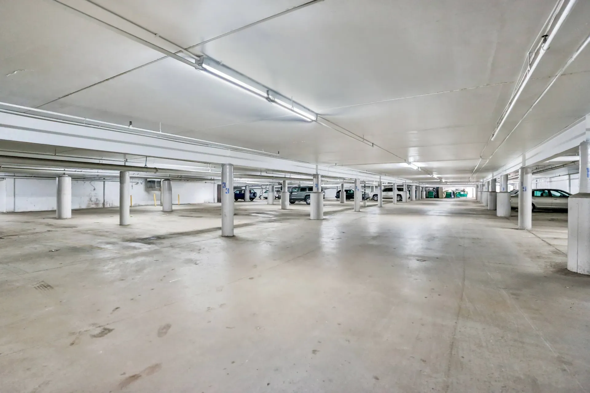 An empty, white, indoor parking garage with several cars parked in the distance.