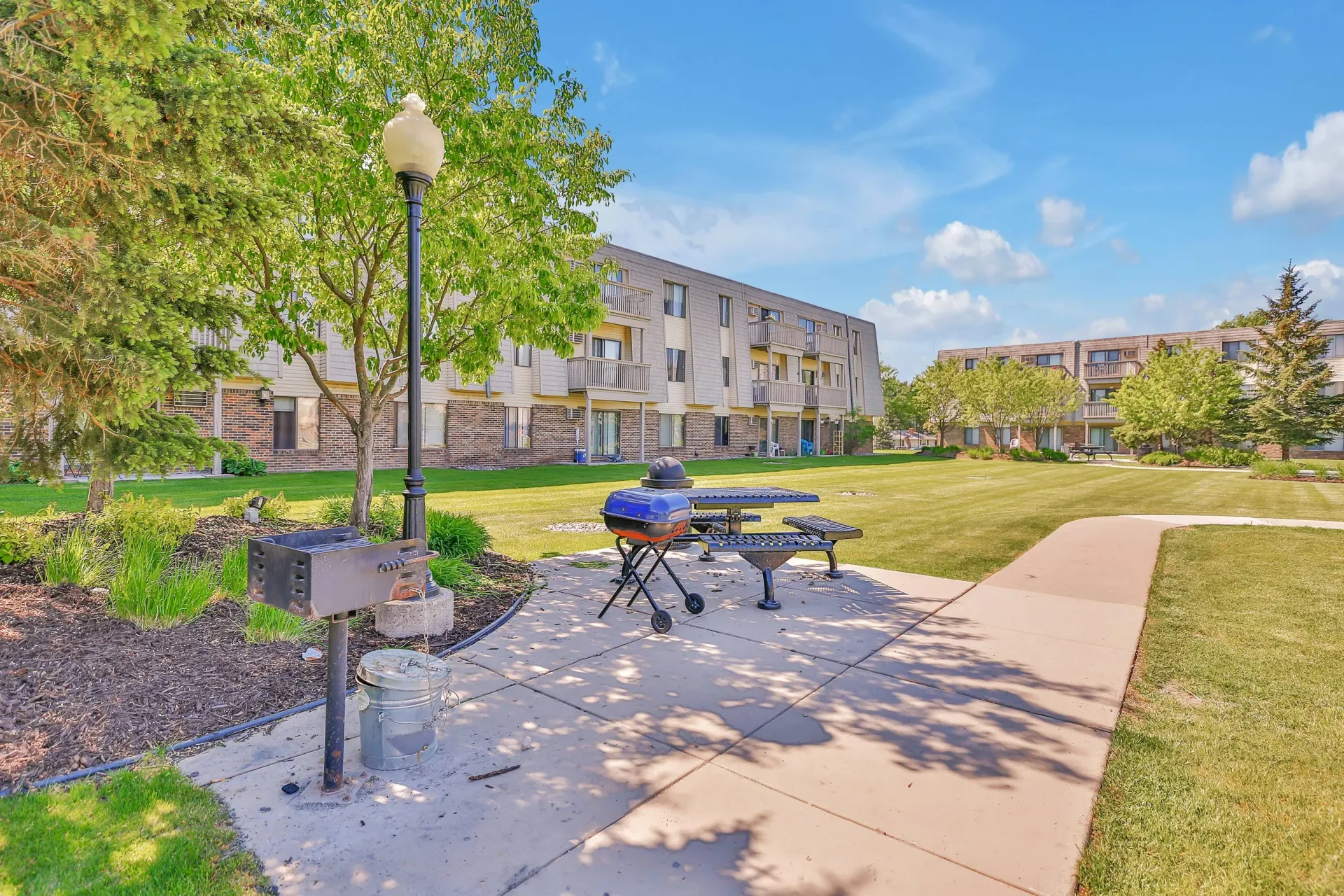 Outdoor communal courtyard at an apartment complex with a grill, picnic table, and green lawn.