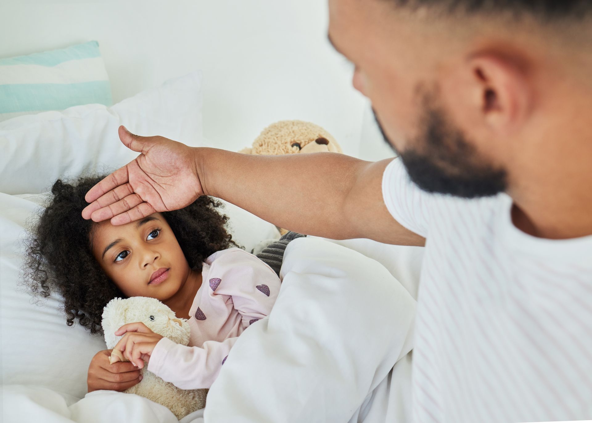 A man is taking the temperature of a sick little girl in bed.