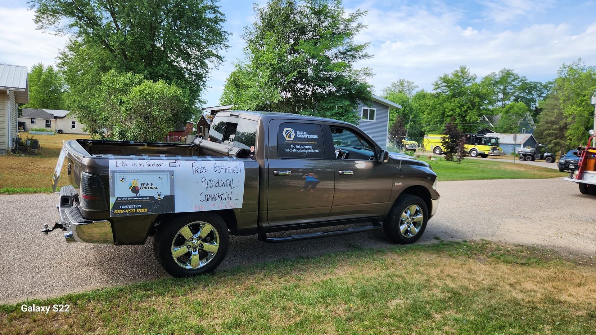Brown pickup truck with a white canopy parked on grass, beside a tree and tents at a campsite.