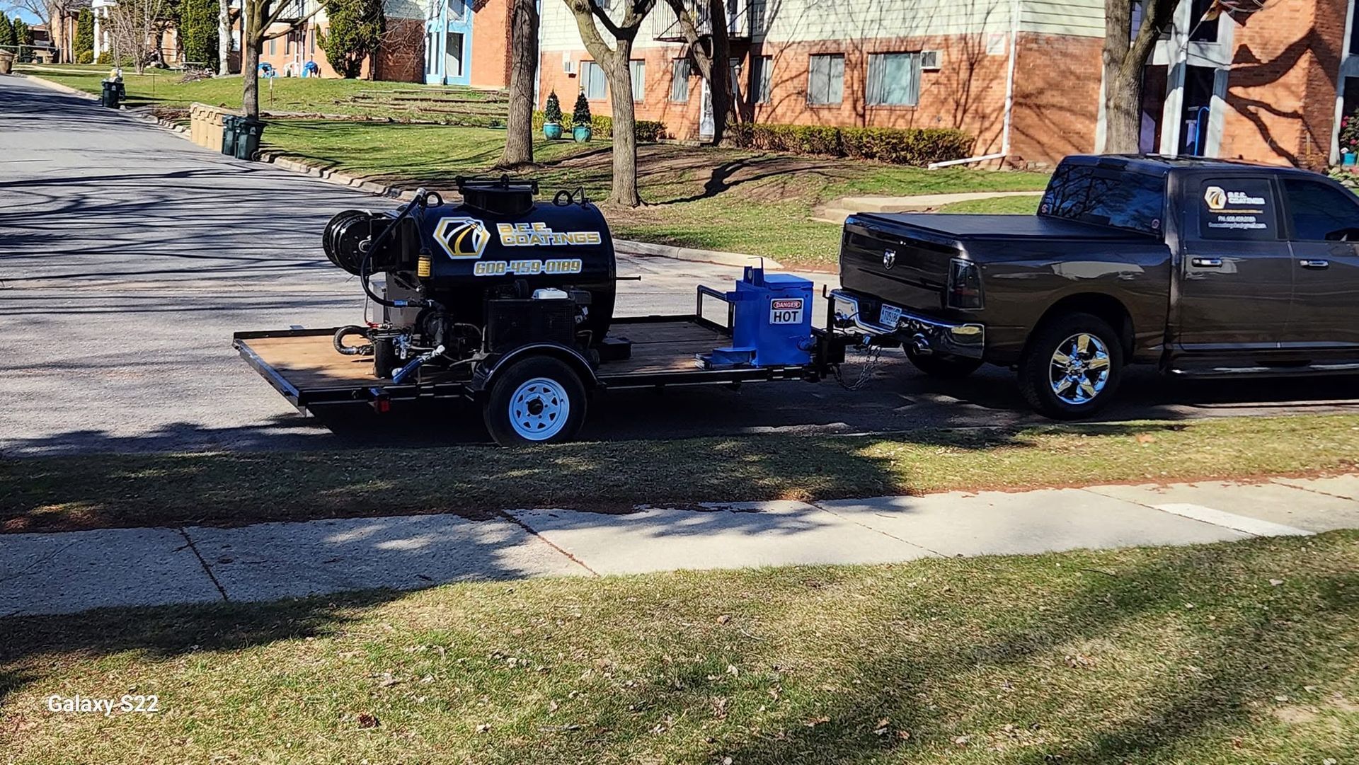 Black pickup truck towing a small black trailer and grill along a suburban street.
