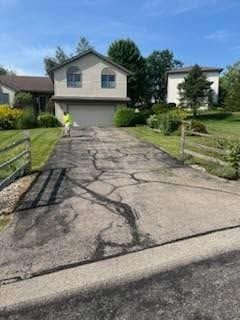 Cracked driveway leading to a two-story suburban house with a front lawn and trees.