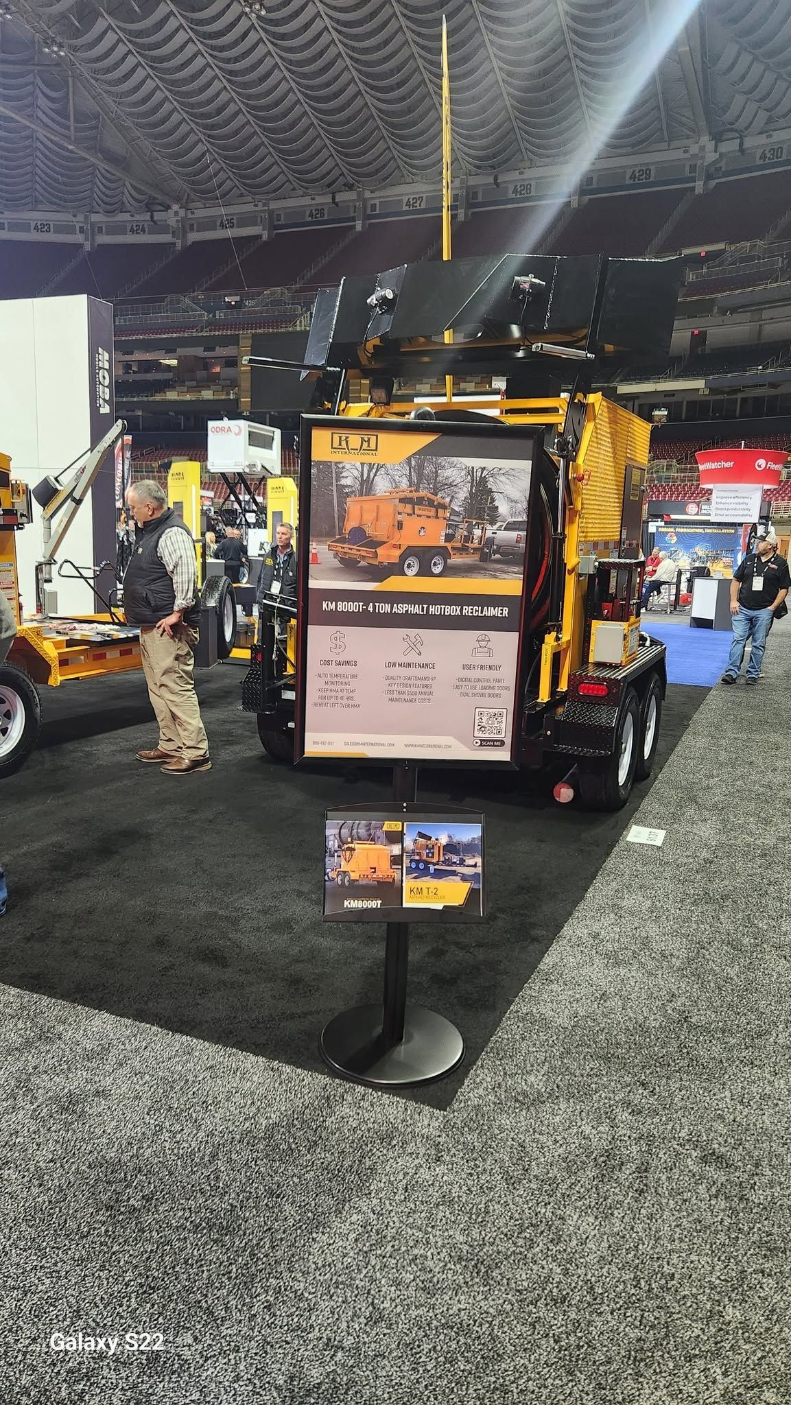Exhibition booth with orange-and-black machinery and a large display sign in an indoor convention hall