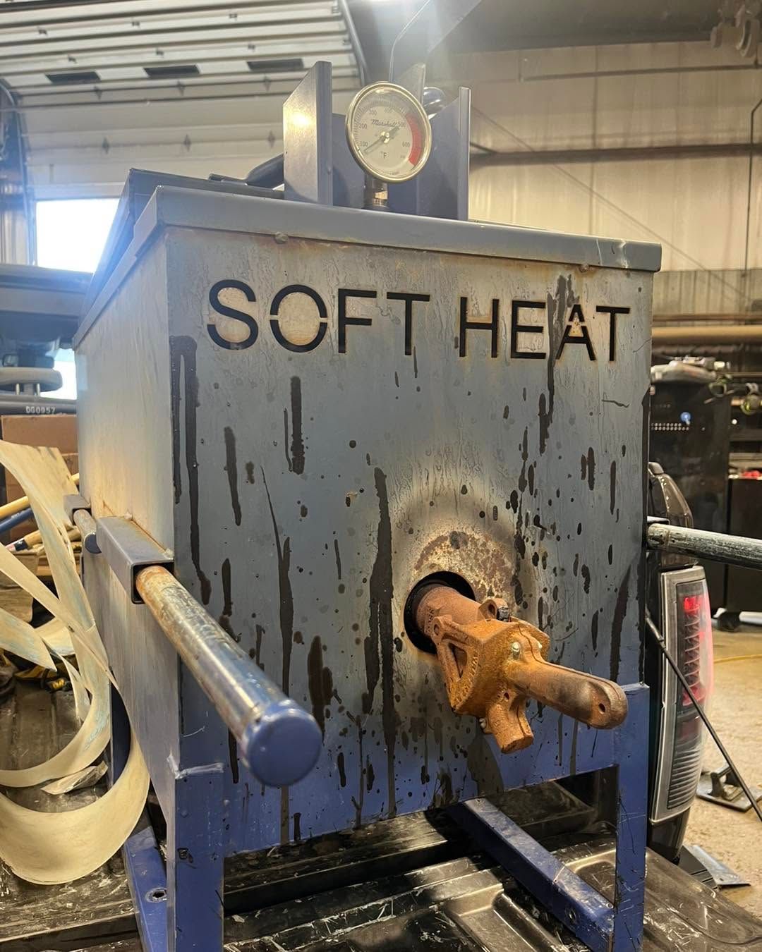 Industrial soft-heat machine with a round gauge and rusted nozzle in a workshop