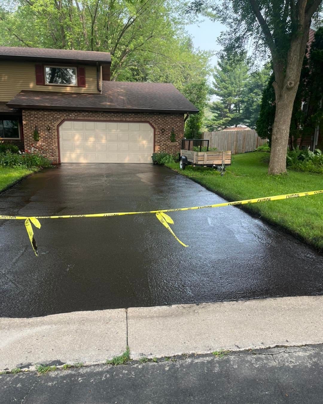 Rainy suburban driveway blocked by yellow caution tape, leading to a two-car garage and wet lawn