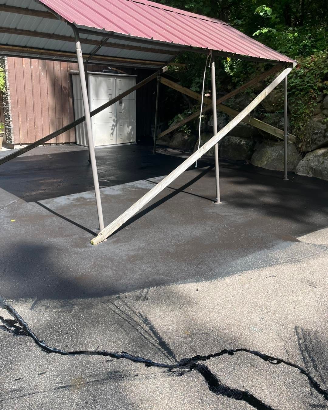 Collapsed carport with a red roof and white support posts leaning over a driveway.