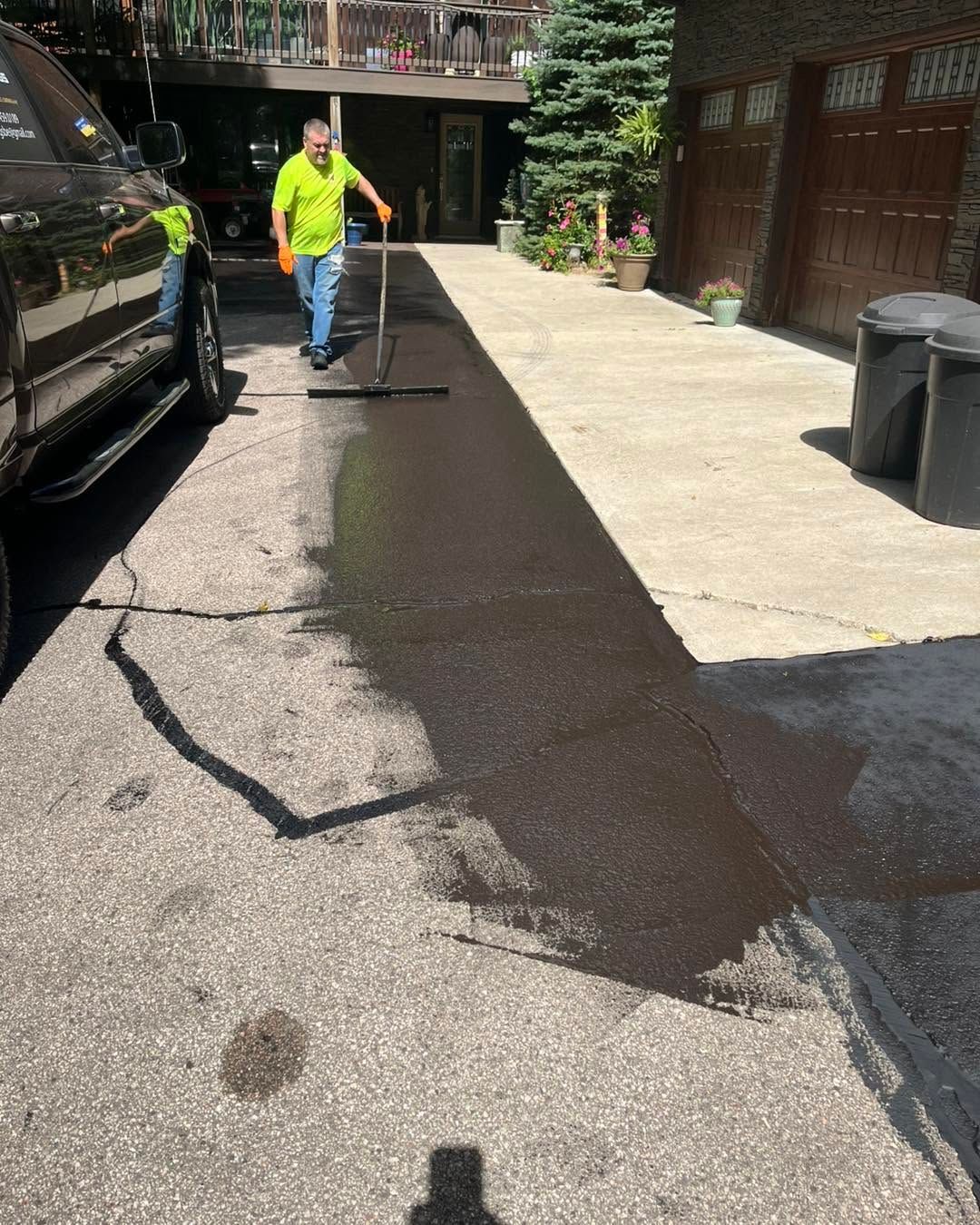 Worker pressure-washing a driveway beside a black car and garage, leaving a dark wet strip