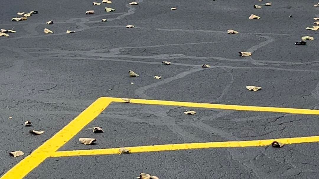 Yellow parking lines on a dark asphalt surface with scattered leaves and small debris.