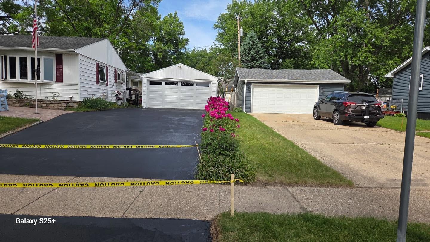 Suburban houses with fresh black asphalt driveway, yellow caution tape, and pink flowers in front yard
