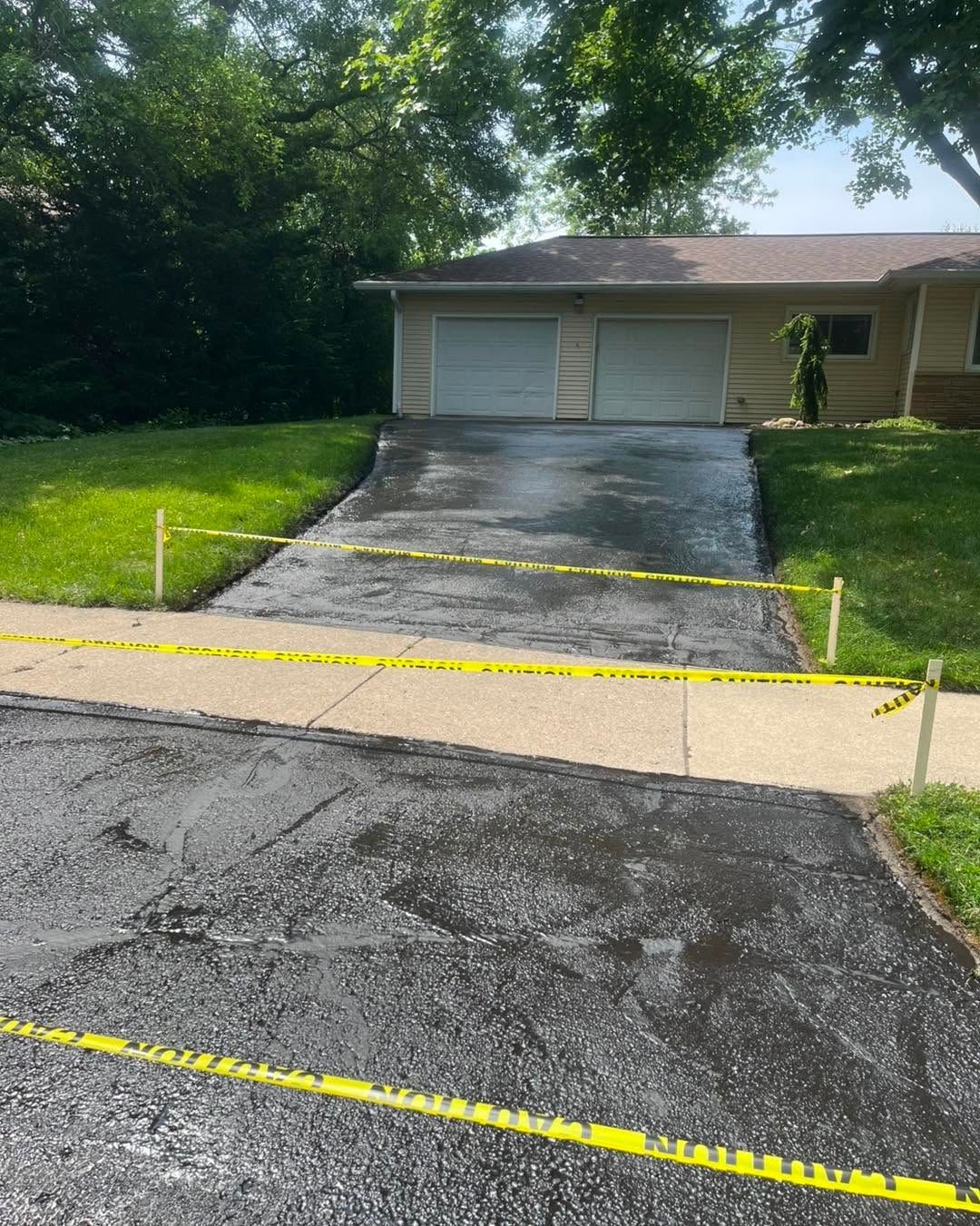 Cracked asphalt driveway with yellow caution tape leading to a two-car garage and house.