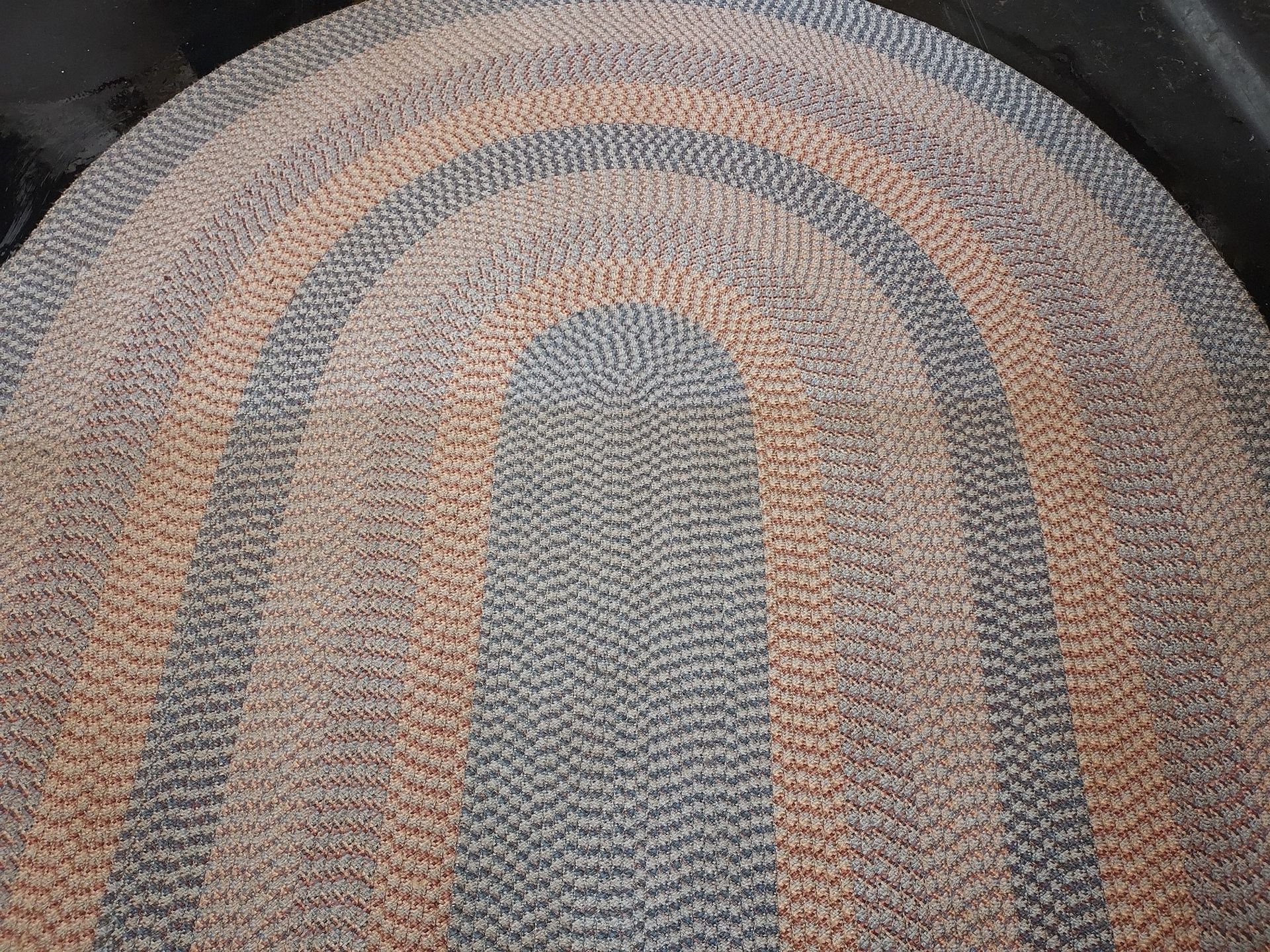 Oval braided rug, alternating rows of grey and peach.