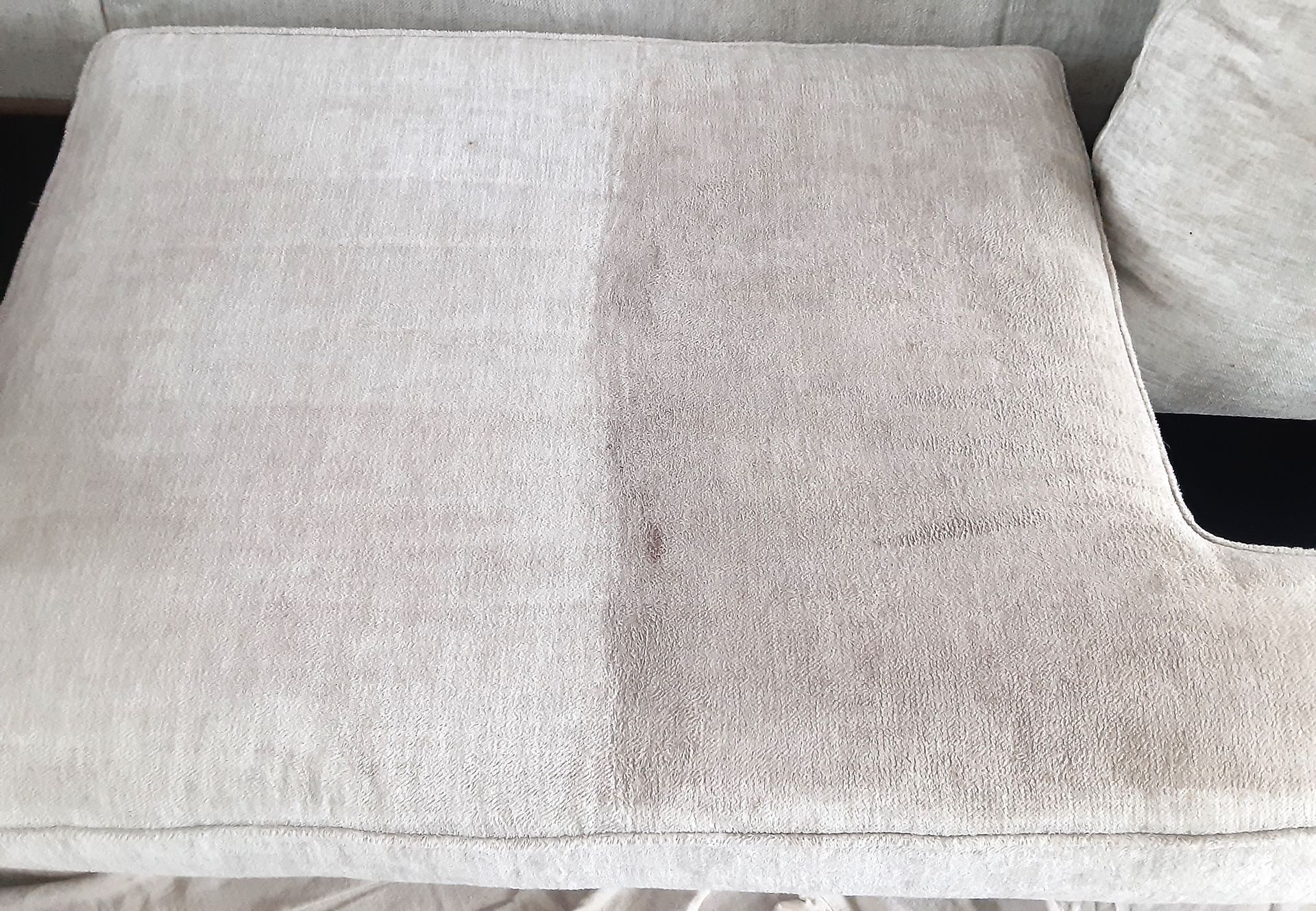A sofa cushion with a light-colored fabric; half is clean, half is stained with dirt.