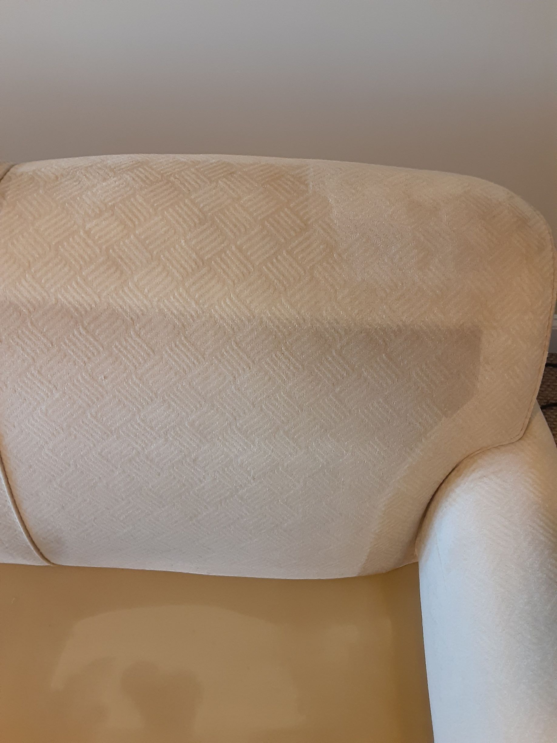 Cream-colored upholstered armchair back and arm, with a slightly textured fabric.
