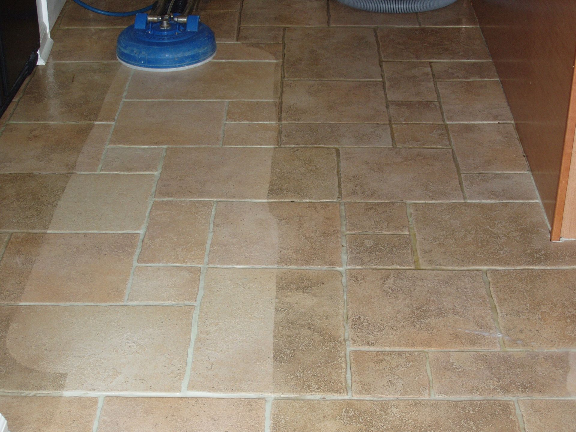 Floor being cleaned; a blue cleaning machine on the left side of the frame creates a wet, clean path on the tile.