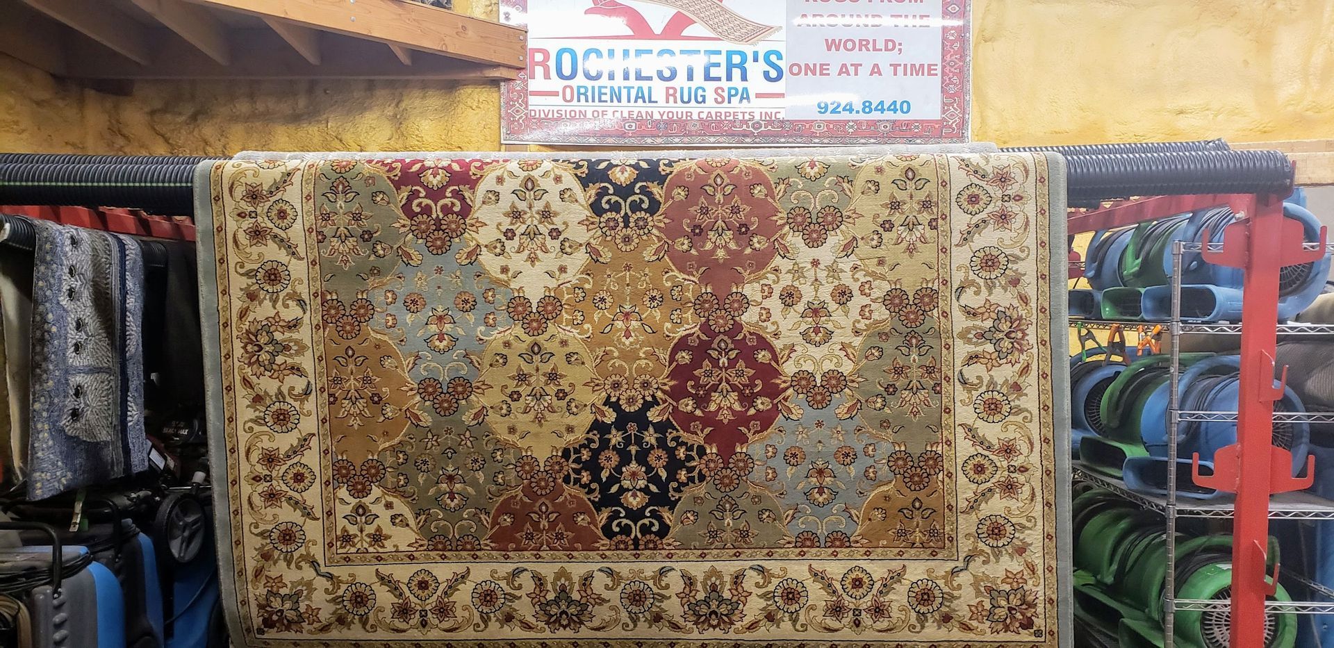 A colorful patterned rug hanging in a rug store, with the store's sign visible.