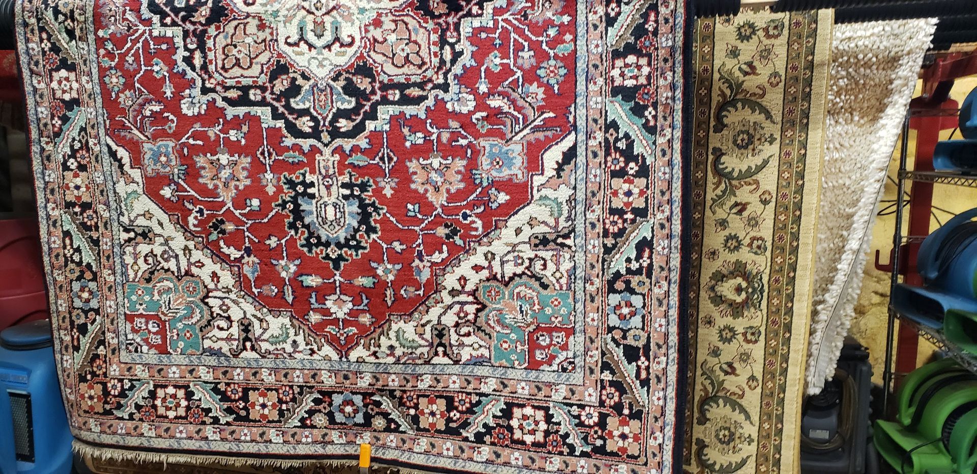 Red and cream patterned rug displayed alongside rolled beige and patterned rugs.