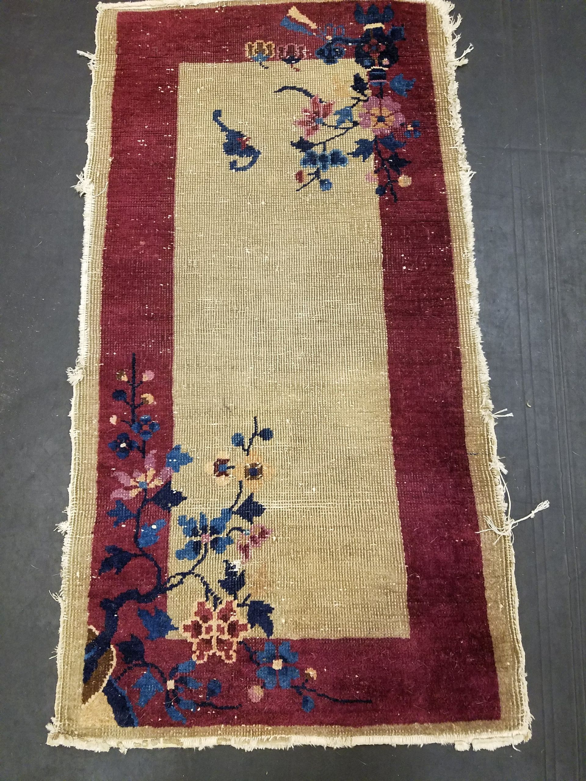Rectangular beige rug with a maroon border and floral designs in pink and blue.