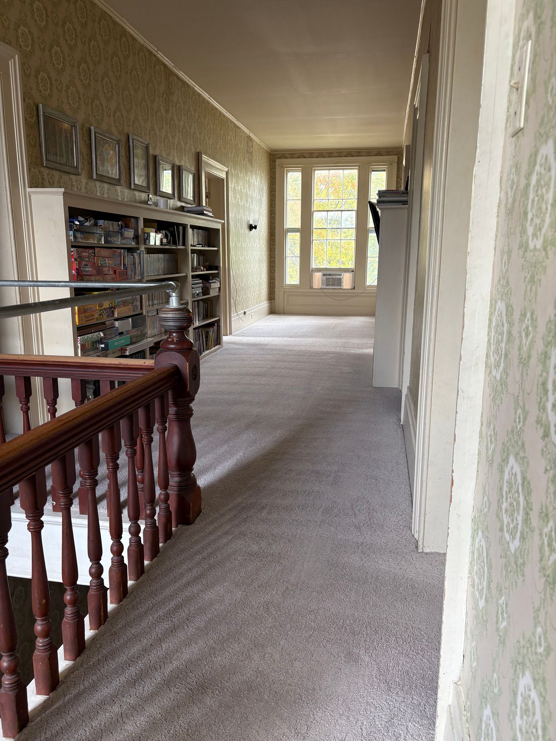 Hallway with carpet, built-in bookshelves, and a stairway with a wooden railing.