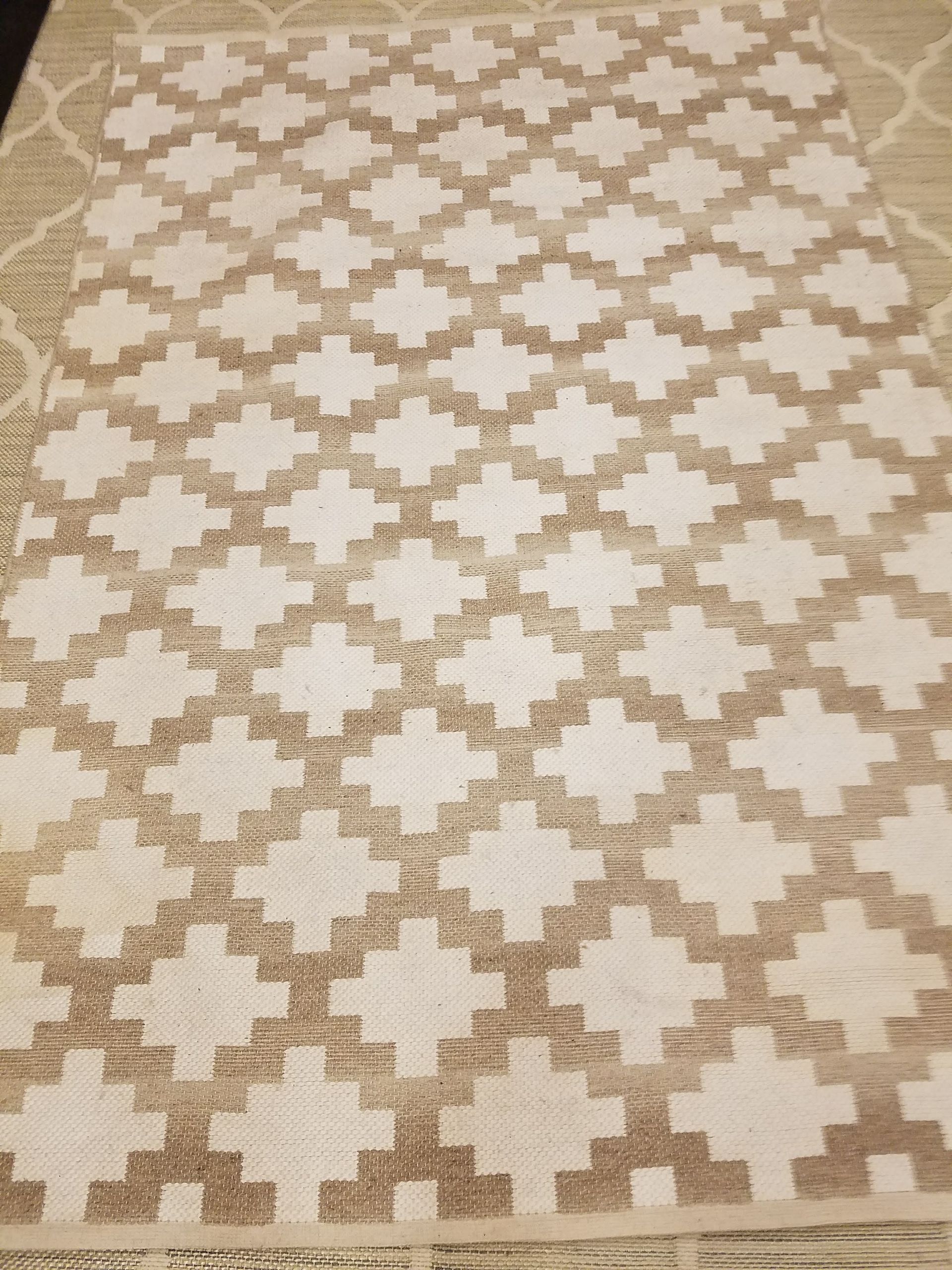 Beige and cream geometric patterned rug on a lighter neutral rug.