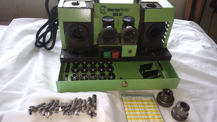 Green industrial machine with controls and parts laid out on a table, in a workshop setting