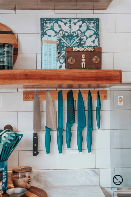 Kitchen wall with wooden shelf, hanging knives, and teal decor on white tile backsplash
