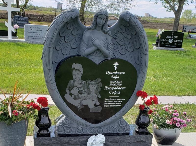 A gravestone in a cemetery with a heart shaped statue of an angel holding a child.
