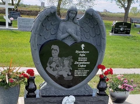 A gravestone in a cemetery with a heart shaped statue of an angel holding a child.