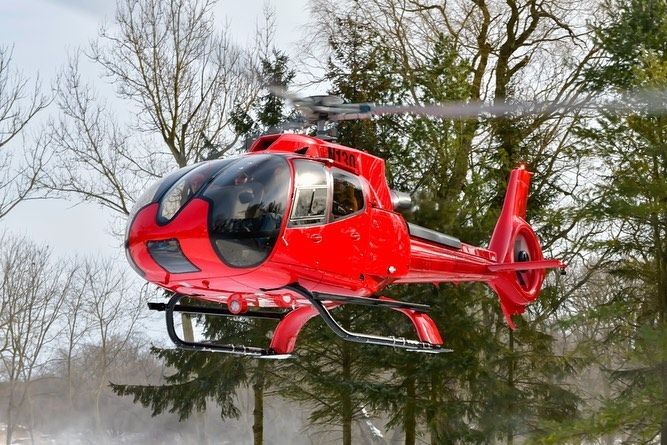 Red helicopter in flight near trees.