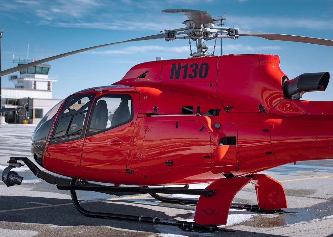 Red helicopter parked on a snow-covered landing pad with a control tower in the background.