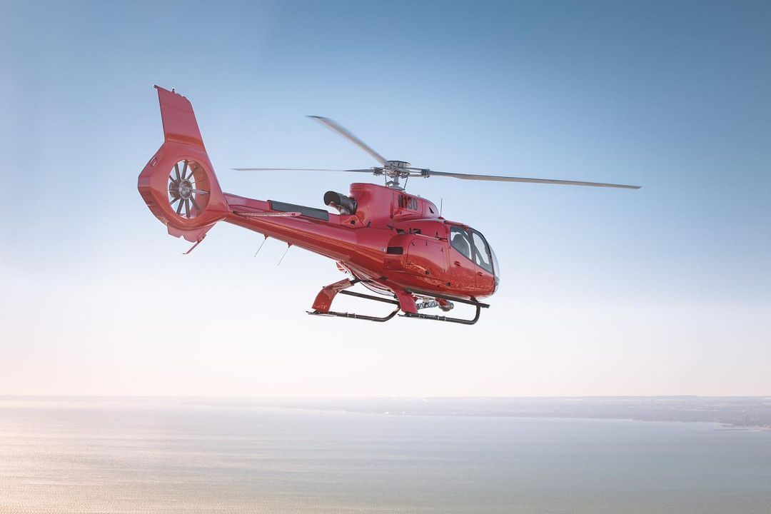 Red helicopter flying over water.