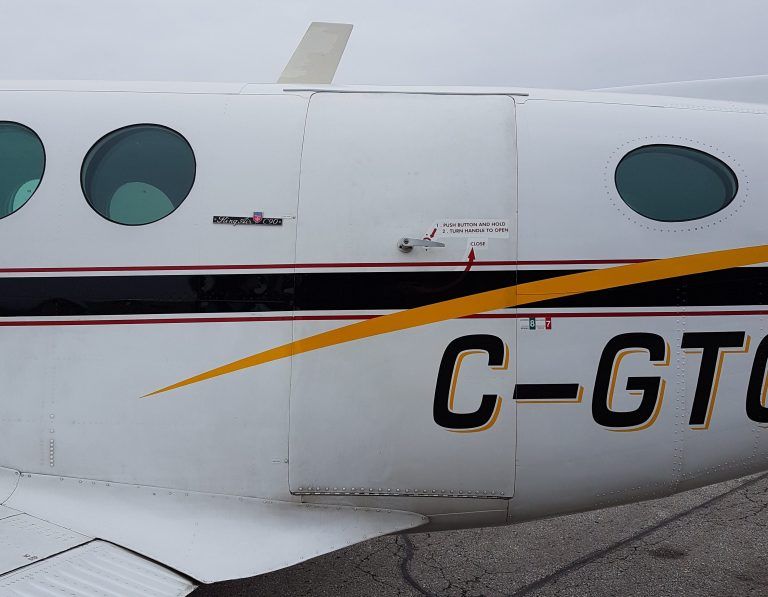 White airplane fuselage with black and gold stripes, round windows, and