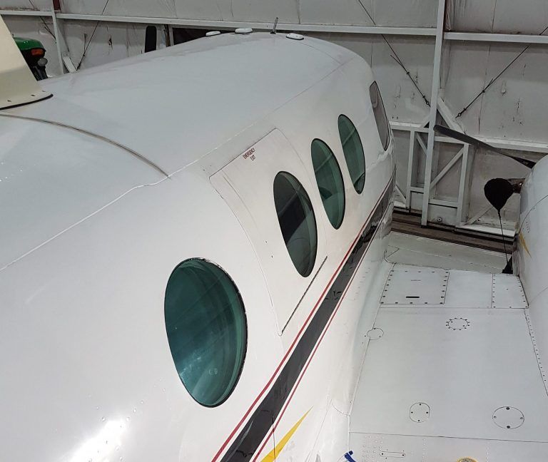 White aircraft fuselage with oval windows in a hangar.