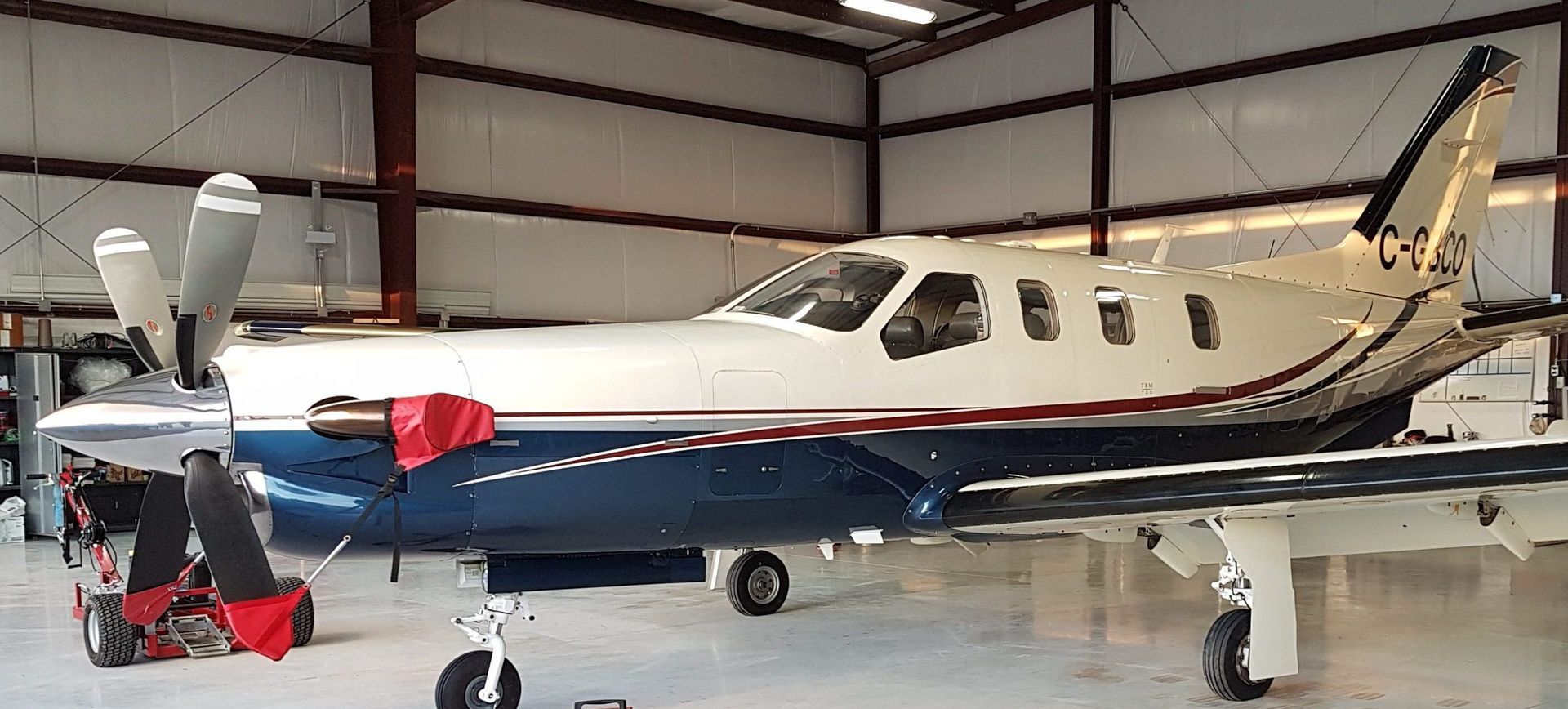 A turboprop aircraft parked inside a hangar. The plane is white and blue with a red cover.
