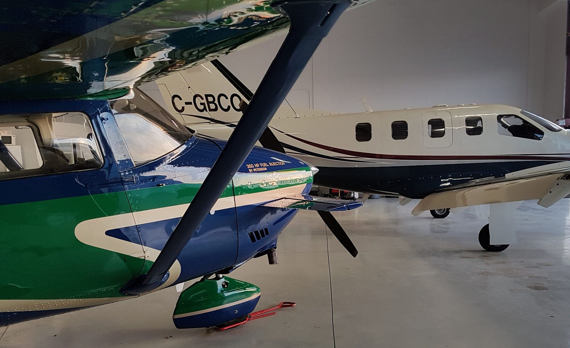 Two airplanes parked in a hangar. One is blue and green, the other is white and blue.