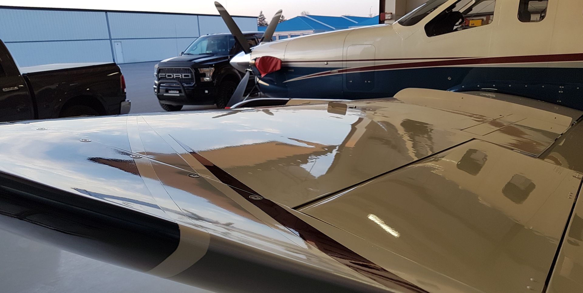 Airplane wing reflecting a vehicle and building. Black truck parked next to the plane on tarmac.