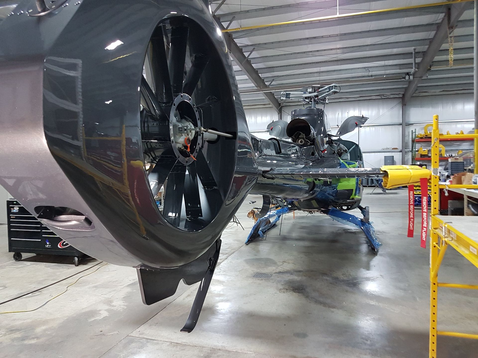 A dark gray helicopter in a hangar with a tail rotor.