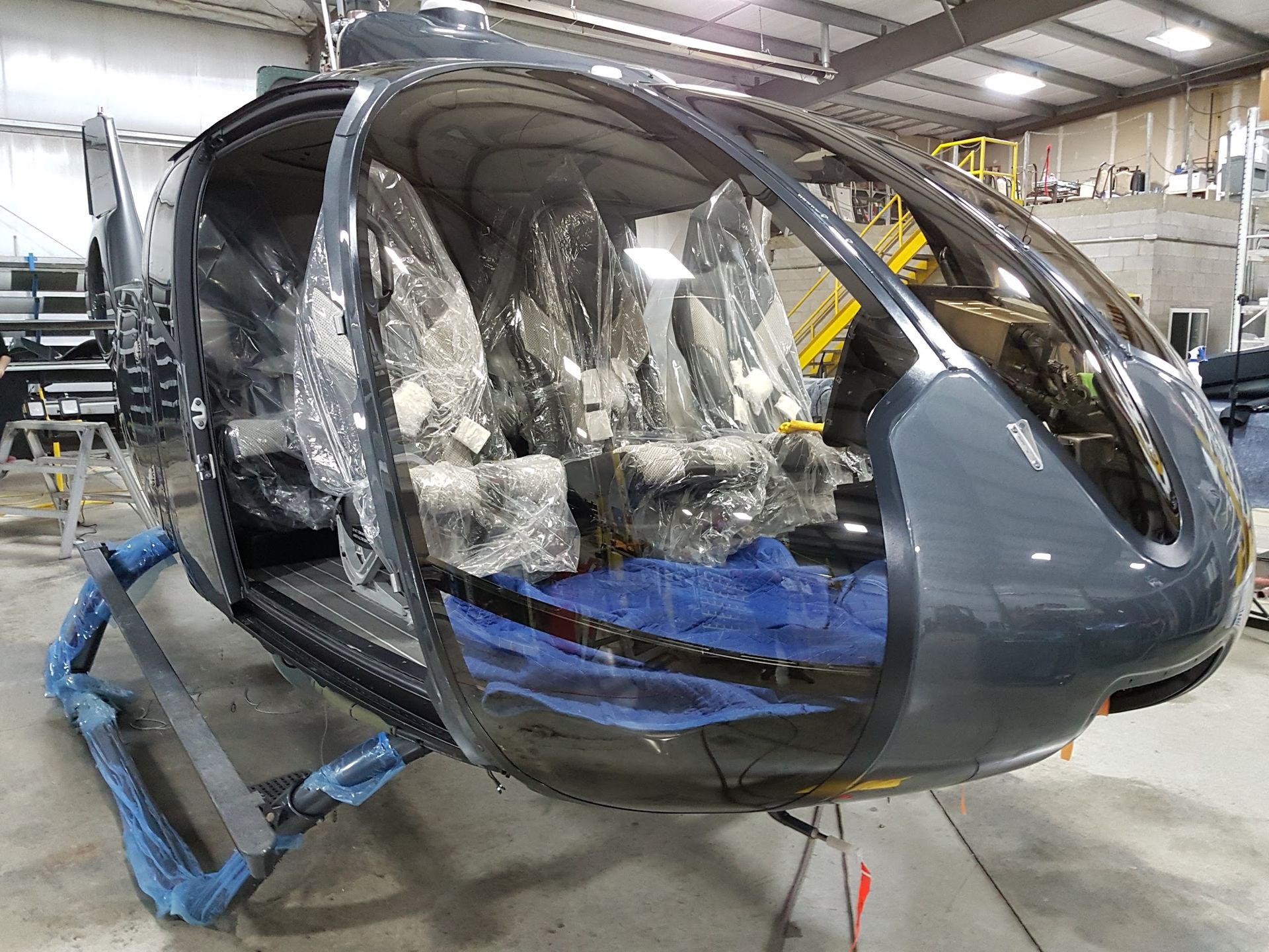 Dark gray helicopter cabin interior with seats wrapped in plastic, in a workshop setting.