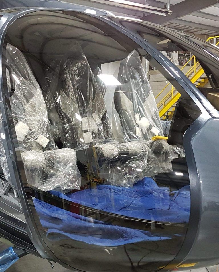 Helicopter cabin interior with seats covered in plastic wrap, viewed through the windshield.