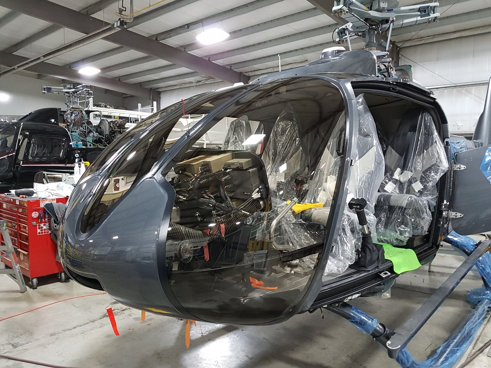 Partially assembled gray helicopter in a hangar; interior visible, covered in plastic.