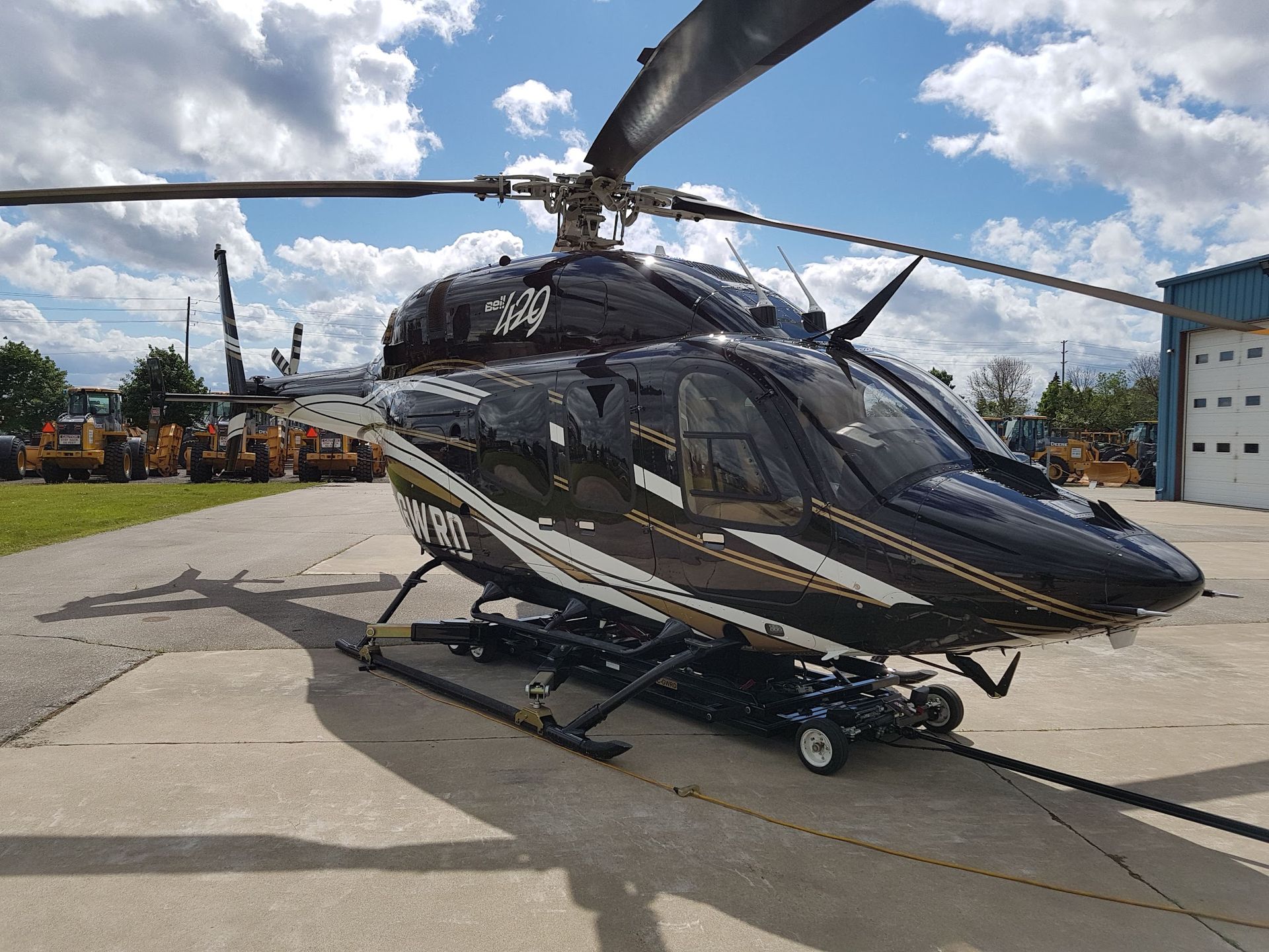 Black helicopter on the ground, with white and gold stripes. Sunny, outdoor setting.