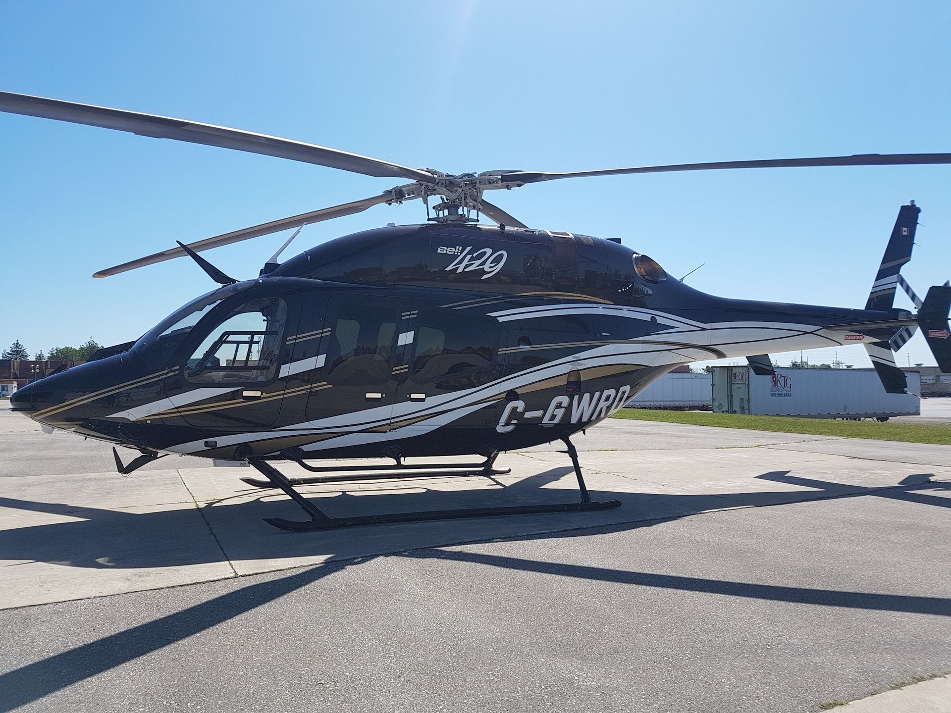 Black helicopter on a paved surface, blades spinning, clear sky. C-GWRP on side.